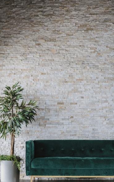 A green couch and plant against a brick wall.