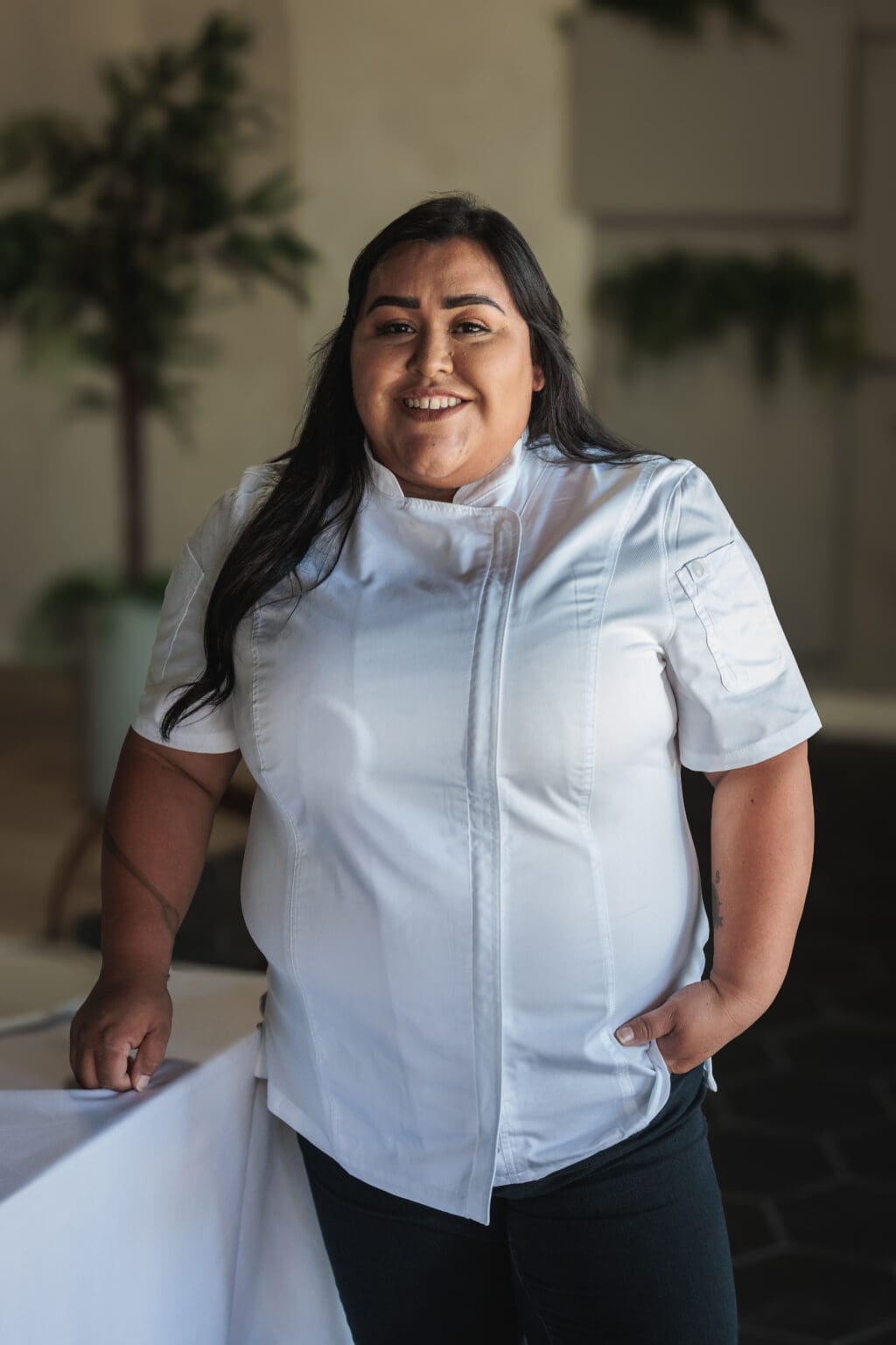 A woman in white shirt standing next to plant.